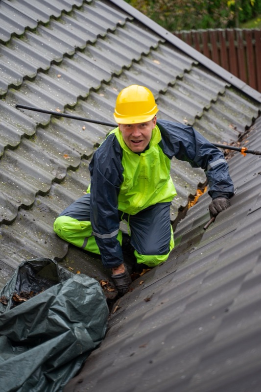 Roofer clearing debris from a roof valley and gutter line